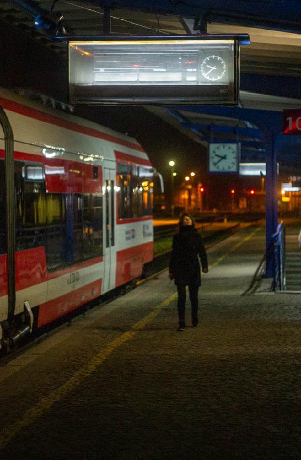 Picture of a girl standing on train station, looking on arrivals table, at night.